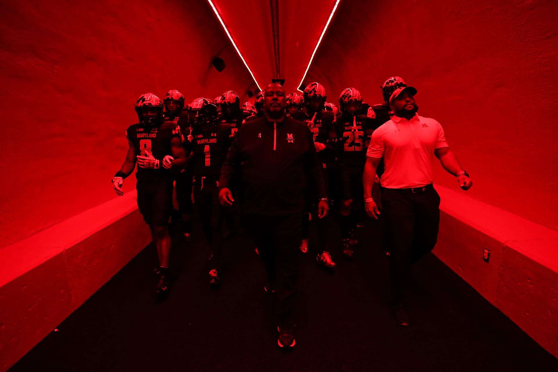 The Maryland Football team walks down the tunnel with Coach Locksley under red lights.