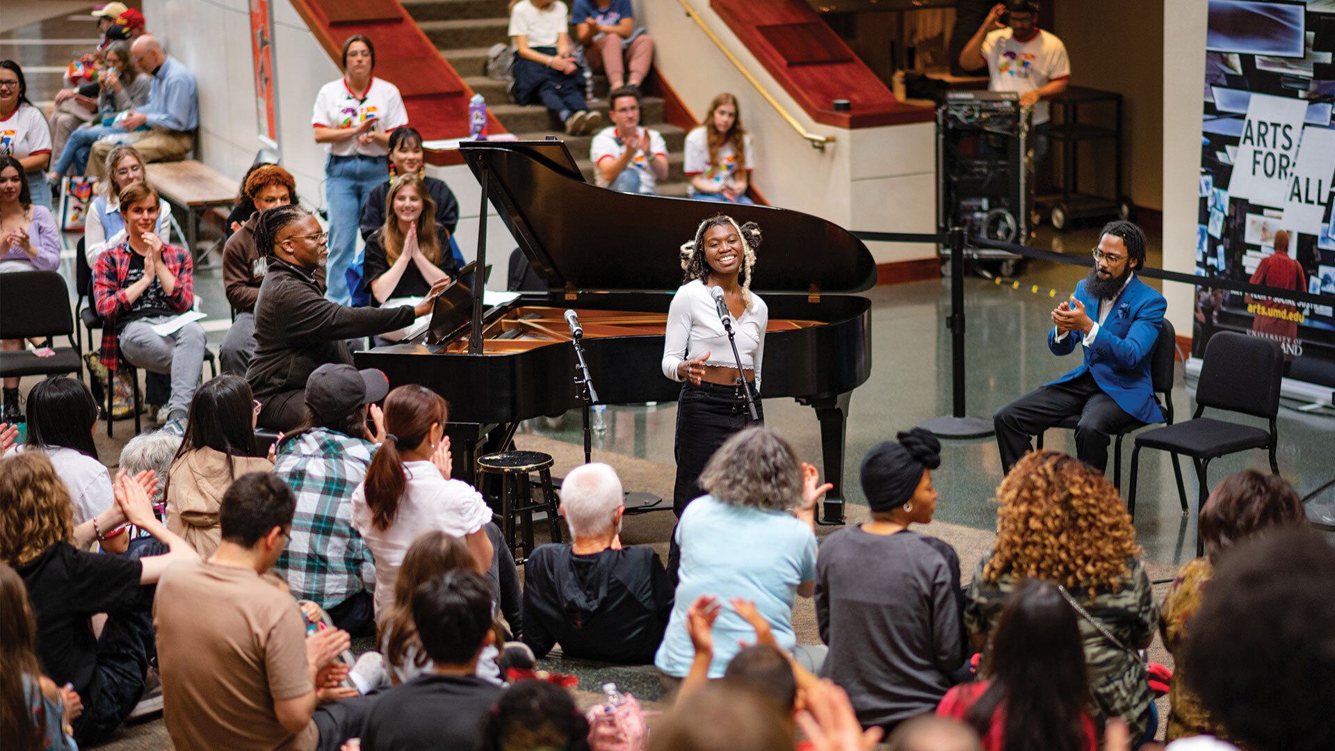student sings while man plays piano and crowd claps
