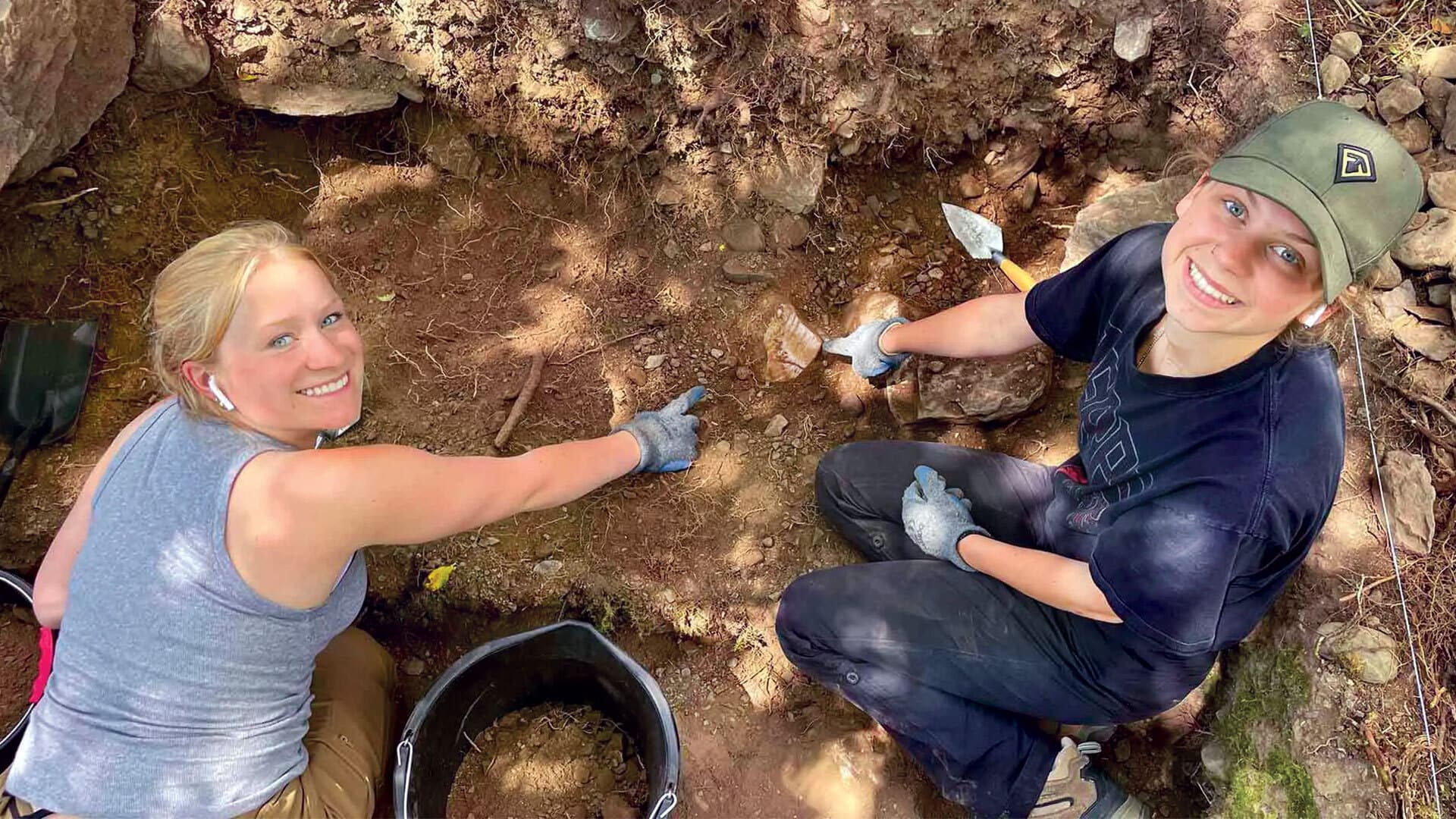 two students point to cream pan they dug up