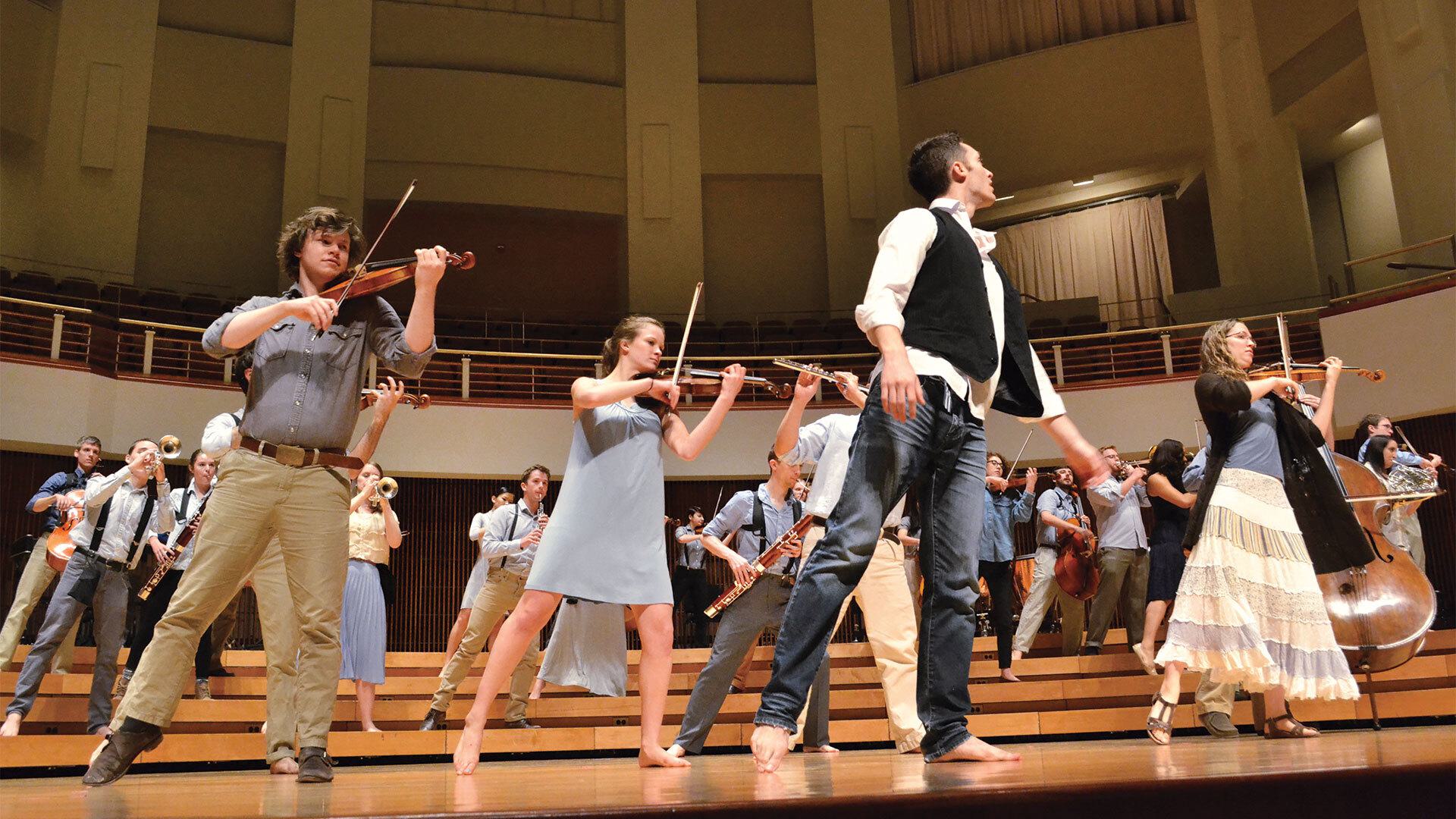 orchestra members dance on stage while playing instruments