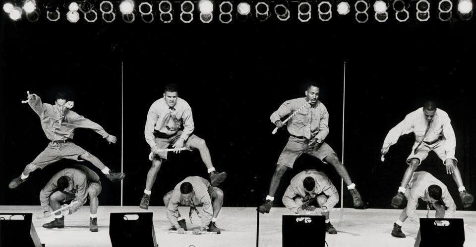 four students leap over four others on stage during step show