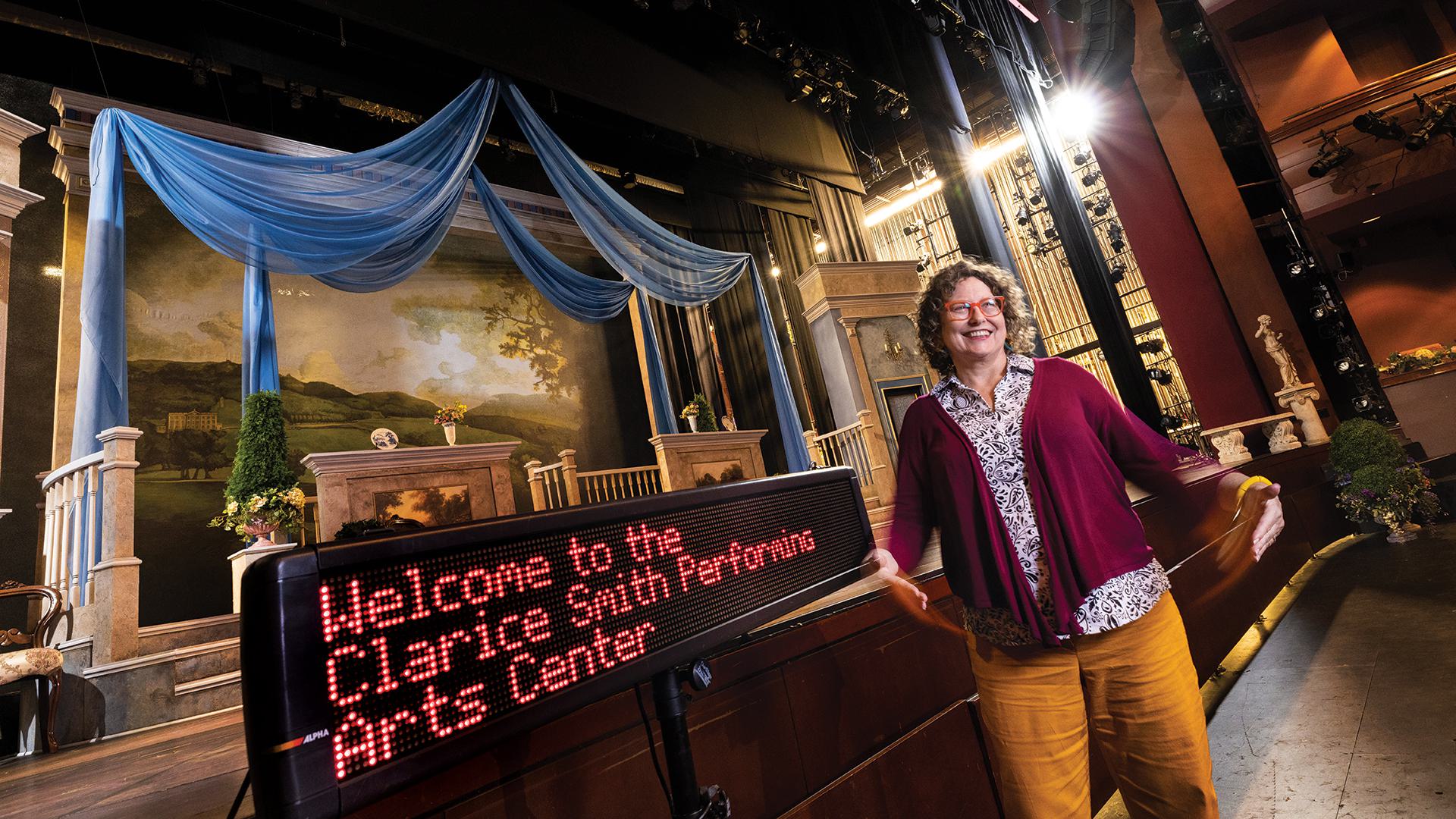 Jill Bradbury signs in front of stage next to electronic sign that reads, "Welcome to the Clarice Smith Performing Arts Center"