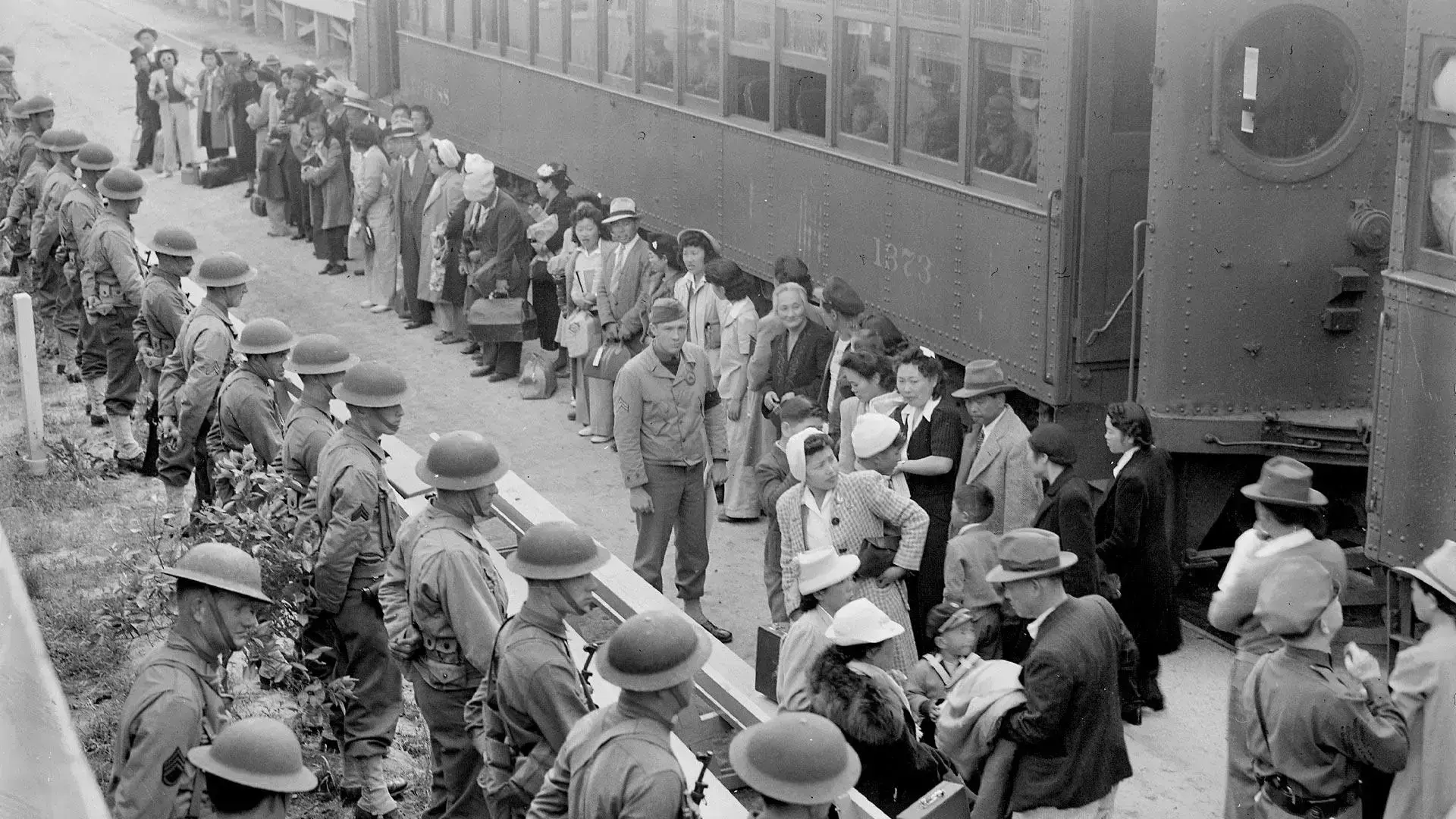 The image depicts a historical moment during World War II in April 1942, showing Japanese Americans arriving by train at the Santa Anita Park assembly center in California.