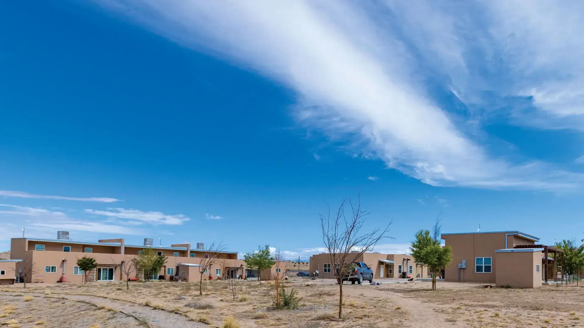 View of low, tan buildings against a large sky. Dessert terrain.