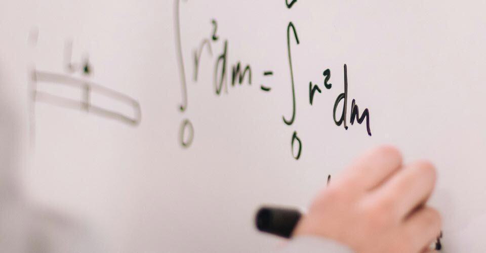 hand writes math formula on whiteboard