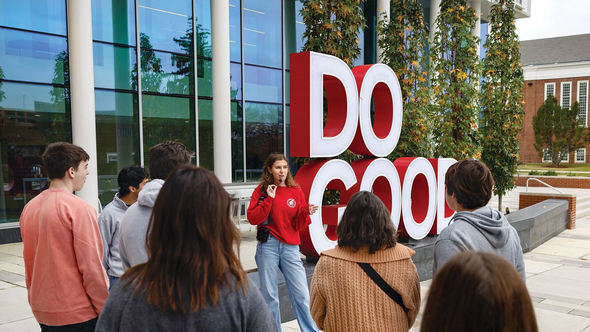 student in red shirt leads tour by Do Good statue