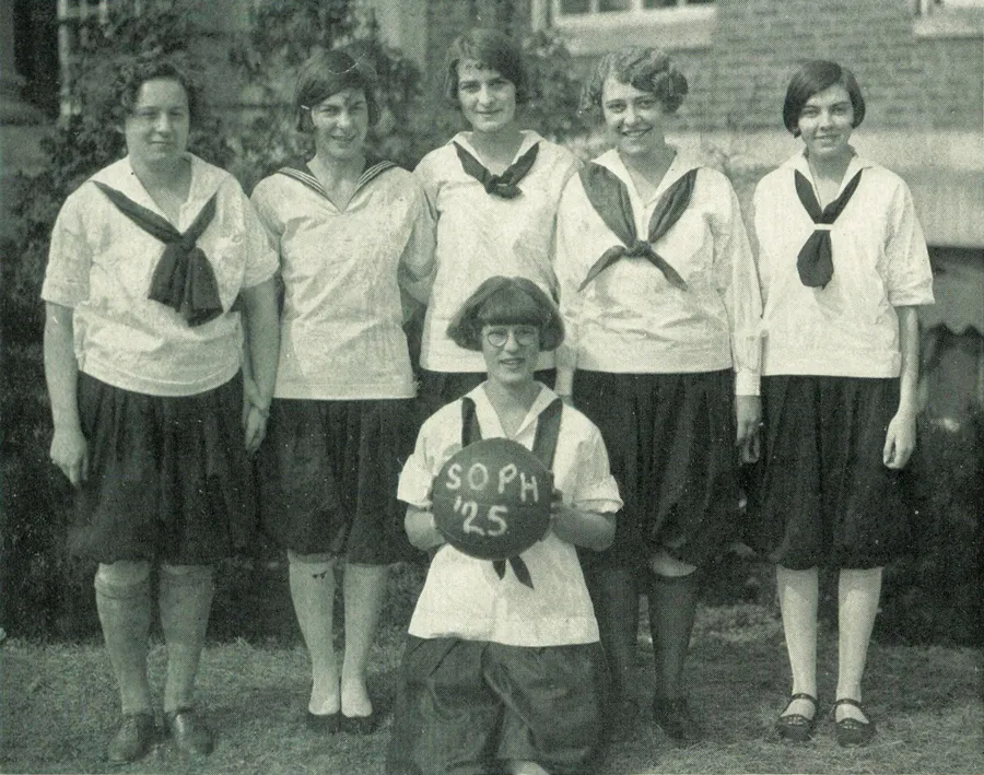 Women in bloomers, Middy blouses with ties and rolled-up hose; one holds basketball reading, "SOPH '25"