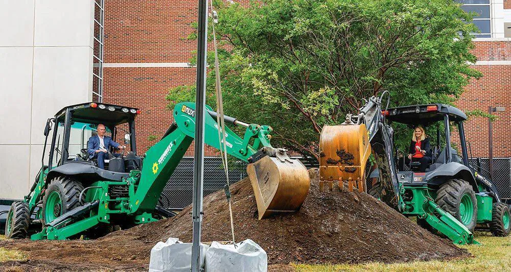 Kevin Willard and Brenda Frese behind wheels of excavators