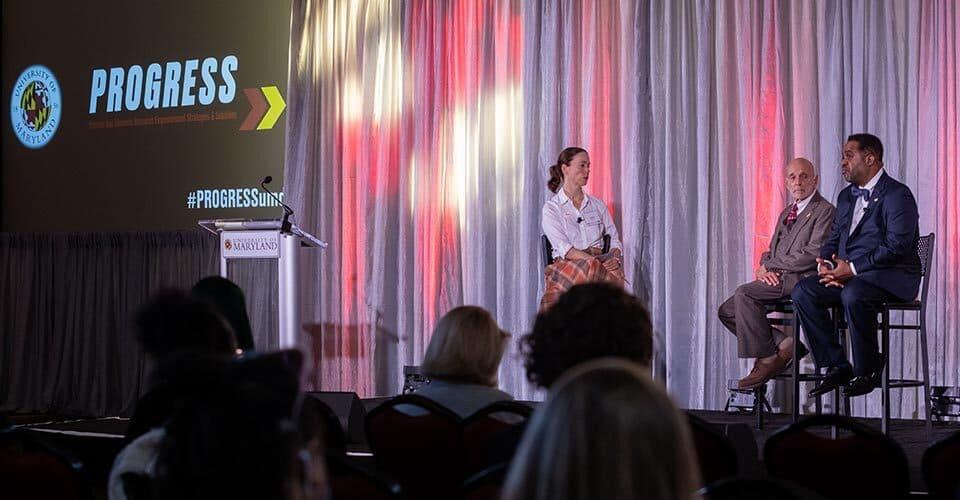 three people sit on stage at PROGRESS launch